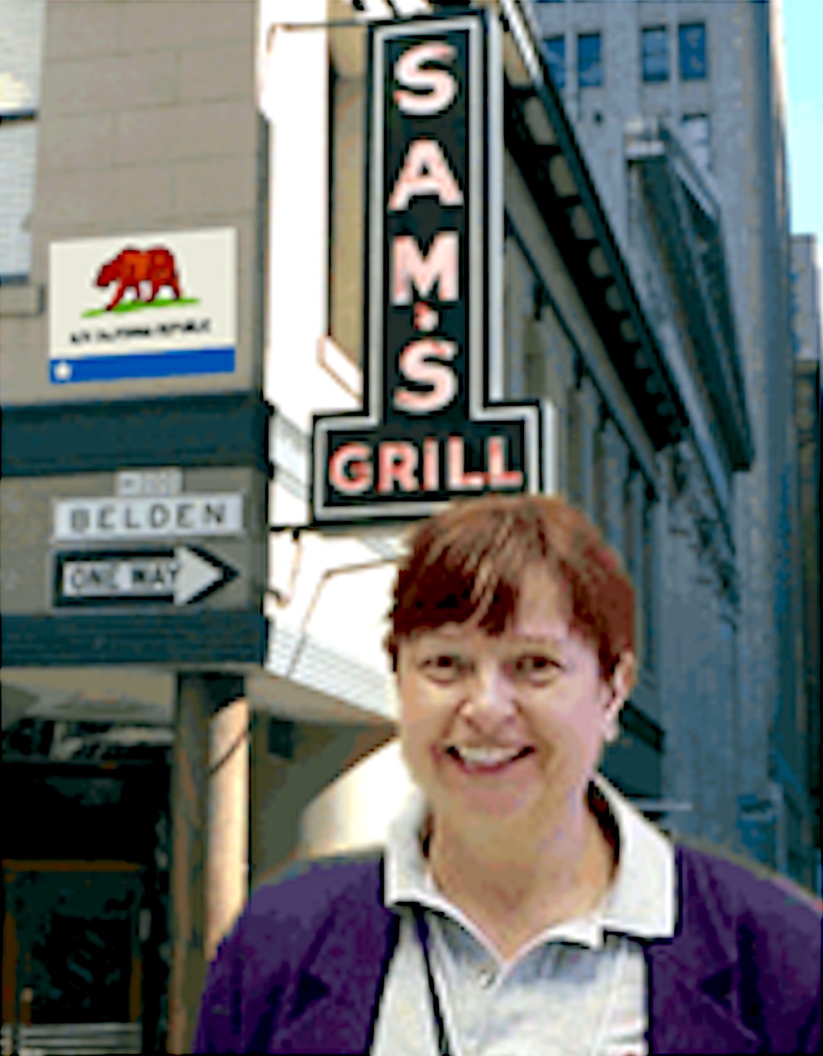 Beth’s headshot from the back cover of her satirical lesbian time-travel novel, Don’t Call It Virtual, 2003, San Francisco, CA. Beth shares, “Sam’s Grill, and the stamp and coin store around the corner, would still be there in my fictional 2064 San Francisco… which, per the alt Bear Flag, would be the capital of the Alta California Republic.” Photo courtesy of Beth Elliott.