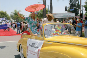 Jewel and her wife Rue Thais-Williams waving and pointing to the crowd while riding in WeHo Pride, West Hollywood, CA. The white sign on their yellow car reads, “Jewel Thais-Williams: Andelson/Thais-Williams Business Award”.  Photo courtesy of Jewel Thais-Williams.