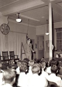 Charles Silverstein speaking to high school students in their auditorium, 1950.