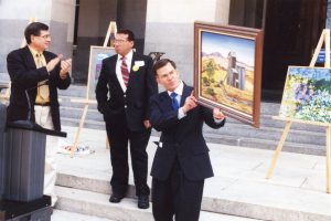 L-R: Dr. Michael Clark and Assemblyman Roy Ashburn on the State Capital steps, Sacramento, CA, 1999. Roy displays original artwork created by clients of the Kern Regional Center. Photo courtesy of Roy Ashburn.