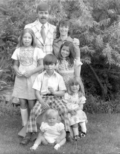 This is a photo of Gary and Millie and the “first five.”  This was taken in our backyard in Provo, Utah, in autumn of 1975.  Our sixth child, Brian, was not yet born.  Craig is seated in the middle and Lori would have been about 18 months-she is seated on the grass.  Nancy and Becky are standing behind Craig.