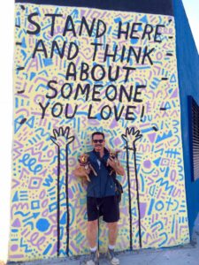 Jolino with his dogs in front of a mural that reads, “Stand Here and Think About Someone You Love!”, Silver Lake, Los Angeles, CA, 2016.