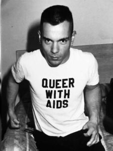 A portrait of Mehmet wearing a shirt that reads, “Queer with AIDS”. Photo courtesy of Mehmet Sander.	