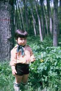A portrait of Mehmet (age 3), holding flowers with many trees and plants in the background. Photo courtesy of Mehmet Sander.