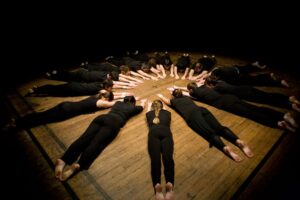 Dancers lying in a circle with their arms outstretched during a Mehmet Sander Dance Company performance rehearsal, 2011. Photo Credit: Bobby Whittaker. Photo courtesy of Mehmet Sander.
