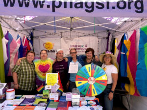 Staff from the Intersex and Genderqueer Reconition Project in a booth surrounded by different pride flags.