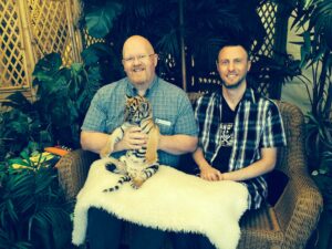 Brett (holding a tiger) with his husband Mike Turay at the Rose Festival Special Needs Day. Brett shares, “Always with pets!”
