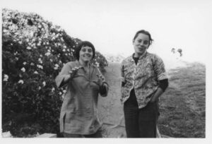 L-R: Judy Abdo and her friend Bernadette from the Church in Ocean Park, smiling and standing next to a bush of flowers, 1970s. Photo courtesy of Santa Monica Public Library Image Archives, Judy Abdo Photo Album Collection.