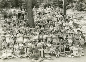 Judy (in front of the tree on left side, wearing glasses) as a camp counselor at one of the “Indian Village” Junior Camps, 1960s. The “Indian Village” Junior Camp was organized by the Forest Home Christian Conference Center in Forest Falls, CA. Participants are in the woods, sitting or standing with their arms crossed in front as a salute. Photo courtesy of Santa Monica Public Library Image Archives, Judy Abdo Photo Album Collection.