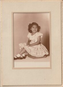A portrait of Terri, age 3, in a white dress, 1950. Photo courtesy of Terri de la Peña.