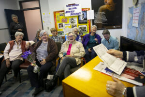 Deborah and Houston Women’s Group members sitting and laughing as group poet laureate Dr. Jacsun Shah shares at the podium, Houston, TX, 2020. Photo courtesy of Deborah Moncrief Bell.