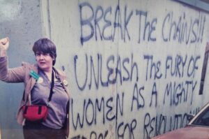 Deborah, as an activist for the National Organization for Women (NOW), poses with her fist raised during a march in Washington, D.C. The background wall reads, “Break The Chains!! Unleash The Power Of Women As A Mighty Force For Revolution!!” Photo courtesy of Deborah Moncrief Bell.