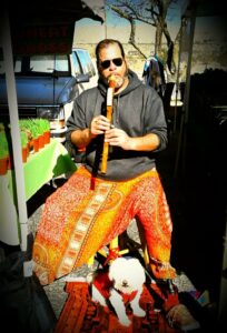 Miguel playing a Native-American flute at the Saturday Farmer’s Market with Chico sitting underneath him, Joshua Tree, CA, 2016. Photo courtesy of Miguel Criado.