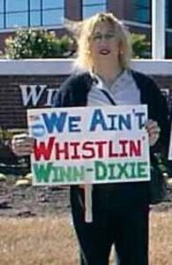 Monica (age 49) protesting Winn-Dixie and  holding a sign that reads, “We Ain’t Whistlin’ Winn-Dixie” in front of the store, 2001. The protest was related to the firing of Peter Oiler, a former Winn-Dixie employee who cross-dressed. Photo courtesy of Monica Helms.