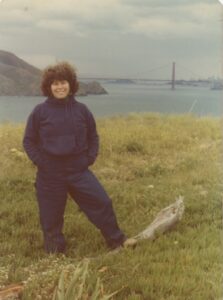 Judith posing in the Marin Headlands with the Golden Gate Bridge in the distance, Sausalito, CA, 1976. Photo courtesy of Judith Masur.