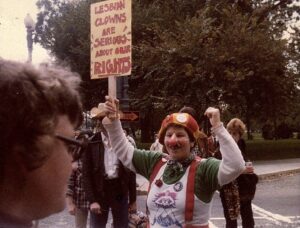 Judith dressed as Prosciutto the clown, holding a poster that reads, “Lesbian Clowns Are Serious About Our Rights!”, Washington, DC, 1979. Photo courtesy of Judith Masur.