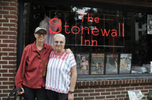 L-R: Barbara Byers (Margaret’s partner) and Margaret Randall smiling in front of the Stonewall Inn, New York City, NY, 2011. Photo courtesy of Margaret Randall.