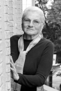 A portrait of Margaret leaning against a brick wall. Photo Credit: Pascual Borzelli. Photo courtesy of Margaret Randall.