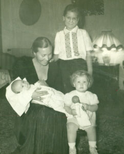 Esther (right) holding a doll, her mother (left) holding her sister Brigette and smiling towards Esther, and her brother David (standing above Esther) smiling at the camera in Belgrade, Yugoslavia, 1956. Photo courtesy of Esther Rothblum.