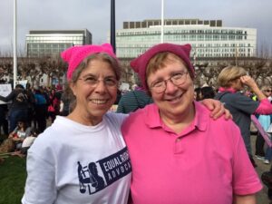 Esther Rothblum and her partner Penny Sablove hugging and wearing pussyhats at the San Francisco Women’s March, 2019. Penny’s shirt reads, “Equal Rights Advocacy.” Photo courtesy of Esther Rothblum.	