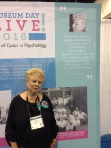 Oliva standing in front of a banner that acknowledges her contributions to psychology during the 2016 American Psychological Association conference. The quote (at right) reads, “Life stories, although deeply personal, also have important personal and psychological purposes: They allow us to… become part of the public world by participating in the process of its making.” Photo courtesy of Oliva Espín.