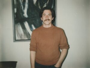 Chuck standing in front of a painting, 1982. Photo courtesy of Chuck Forester.