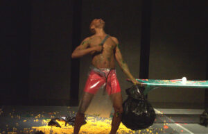 Paul performing in Berserker at Highways Performance Space and Gallery in Santa Monica, CA, 2004. He’s standing with a machete pressed to his paint-splattered chest on a floor strewn with neon-yellow popcorn. Paul shares, “Berserker was named Best Male Performance Solo at the San Francisco Fringe Festival and is also featured as Part VIII in the anthology Blacktino Queer Performance (2016).” Photo credit: Ray Busmann. Photo courtesy of Paul Outlaw.