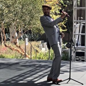 Paul holding the microphone while onstage during the “Becoming Angeleno” segment of the OUR L.A. VOICES Spring Arts Festival, which featured “PROUD Stories,” a celebration of the LGBTQ+ experience in Grand Park, Los Angeles, CA, 2018. Photo credit: Steven Reigns. Photo courtesy of Paul Outlaw.