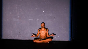 Paul performing in BBC (Big Black Cockroach), a work-in-progress for NOW (New Original Works) Festival at the REDCAT (Roy and Edna Disney CalArts Theater), Los Angeles, CA, 2019. He sits criss-cross in the nude with his hands expressively raised. Photo credit: Vanessa Crocini. Photo courtesy of Paul Outlaw.