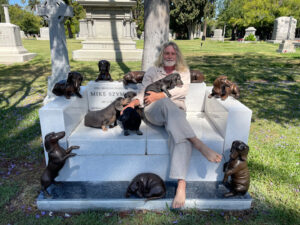 Mike and his dogs posing atop his future tombstone, Hollywood Forever Cemetery, Los Angeles, CA, July 2021. He shares, “After a break-up of a 24 year relationship, I still created a tombstone modeled after my sofa at home and seven past Dachshunds with one future dog in bronze. The four dogs alive at the time are in the photo.” Photo courtesy of Mike Szymanski.