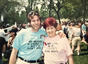 Mike Szymanski and his mother Rose Szymanski in the Pride March, June 29, 1992. Mike’s blue shirt reads, “My mother is straight… but she don’t hate.” Rose’s pink shirt reads, “My son is bi… I don’t ask why.” Photo Credit: activist Lynn Ballen. Mike shares, “This photo is often mis-appropriated on the internet as someone's else's uncle or grandmother. It made the cover of the Bisexual Resource Guide in 2001 and in the collection of iconic LGBT+ photos in ‘We Are Everywhere: The History of Queer Liberation.’” Photo courtesy of Mike Szymanski.