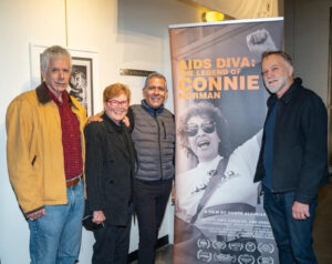 Smiling group photo at the Screening of “AIDS Diva” at LA’s LGBT Center, next to a 7 foot film banner, L-R: Peter Cashman, Torie Osborn, legendary activists and Connie’s friends, Dante Alencastre (in the gray coat), and John Johnston, the film’s co-producer and writer. Los Angeles, CA, November 2022. Photo courtesy of Dante Alencastre.