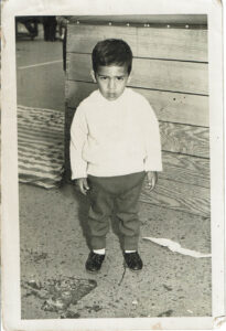 Black and white photo of toddler Dante wearing slicked hair and his favorite patent leather shoes, which he picked himself. Lima, Peru, late 1962. Photo courtesy of Dante Alencastre.