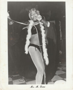 Christy Love performing as “Cat Woman”. She wears black lingerie and sparkly ears, a black robe lined with white fur, and white fishnet tights. The photo is captioned, “Ms. M. Love.” Photo courtesy of Christy Henderson-Jenkins.