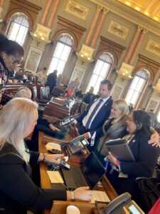 Stephanie Byers (center, gray suit jacket) rejoices with other legislators after the final vote would allow the Governor’s veto of the ban on trans girls in sports to stand at the Kansas State Capitol, in Topeka, Kansas. Photo courtesy of Stephanie Byers.