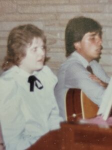 Photo of older teen Lori Haas (L) and Stephanie Byers (R, with guitar) singing together at a wedding, in Norman, Oklahoma, circa 1983. Photo courtesy of Stephanie Byers.