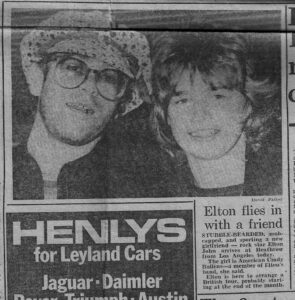 Greyscale newspaper clipping of Cidny Bullens (R) and Elton John (L) on the cover of a London daily newspaper, 1976. The article is titled, “Elton flies in with a friend”. Photo courtesy of Cidny Bullens.