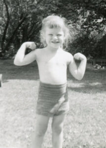 Grayscale childhood photo of Cidny showing his muscles, age 3, 1958. Photo courtesy of Cidny Bullens.