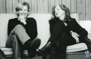 Greyscale photo of Cidny Bullens (L) and Bonnie Raitt (R) smiling backstage at Cidny’s show, San Francisco, CA, 1999. Photo Credit: Joanne Berman. Photo courtesy of Cidny Bullens.