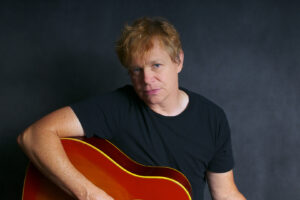 A professional portrait of Cidny holding his guitar (aka his first publicity photo as a trans-man), 2012. Photo Credit: Joanne Berman. Photo courtesy of Cidny Bullens.