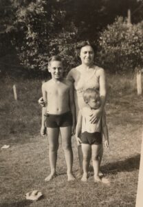 A family portrait of the Gerashes smiling outside in bathing suits, 1936 or 1937. L-R: Walter Gerash (brother), Leah Gerash (mother), and Gerald Gerash (age 3-4, held by his mother). Photo courtesy of Gerald Gerash.