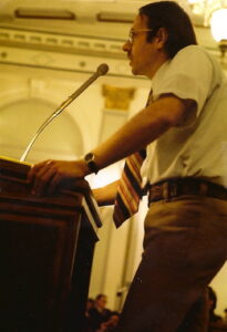 Gerald speaking at a podium during the Denver City Council meeting at City Hall, Denver, Colorado, October 23, 1973. He presented documentation from various court records to show that the only people arrested under 