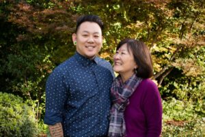 Marsha Aizumi with son Aiden (left) hugging and smiling together in front of a woodsy background; their “You Are My Pride” photo for PFLAG. Pasadena, CA, circa 2019. Photo courtesy of Marsha Aizumi.