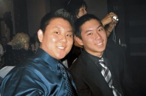 Aiden (left) and brother Stefen Aizumi smiling together in formal shirt and tie suits at a wedding. San Diego, California, circa 2002. Photo courtesy of Marsha Aizumi.