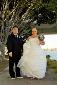 Aiden and bride Mary Aizumi on their wedding day at a river-walk park smiling with a bright paper origami bouquet of flowers. Long Beach, CA, 2013. Photo courtesy of Marsha Aizumi.