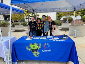 Marsha and Aiden Azumi (two at the center) tabling for “Okaeri: a Nikkei LGBTQ Gathering” with community friends while raising the Pride flag for the first time in Japantown, San Francisco, CA, circa 2022. Photo courtesy of Marsha Aizumi.