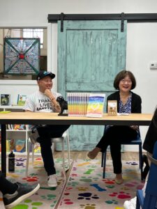 Aiden and Marsha Aizumi smile in front of a stack of their “Two Spirits, One Heart” books, interacting with an audience while speaking at “Underdog Bookstore” in Monrovia, CA, 2023. Photo courtesy of Marsha Aizumi.