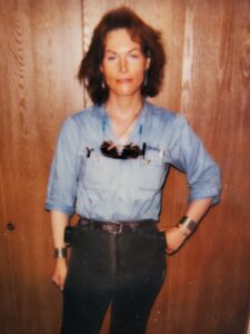 Marsha wearing denim on denim, with shoulder length hair and bangs in front of a 
wooden door. Photograph courtesy of Marsha Botzer. 