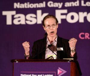 Marsha gives a passionate speech wearing a dark suit and eyeglasses in front of a 
purple “National Lesbian and Gay Task Force” banner on stage, at the Creating Change Conference. Oakland, CA, 2005. Photograph courtesy of Marsha Botzer. 