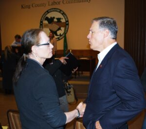 Marsha Botzer shakes hands with Governer Jay Inslee, both wearing dark blue suits, October 2015. Photograph courtesy of Marsha Botzer. 